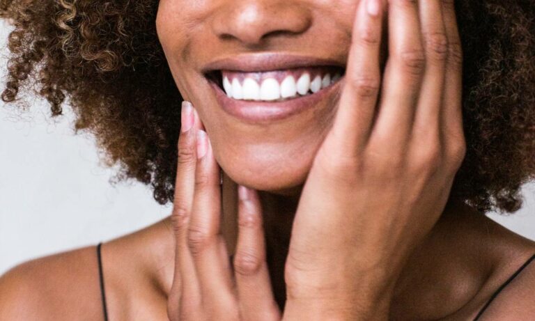 Femme noire souriante avec mains sur visage