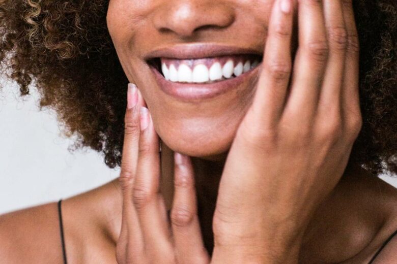 Femme noire souriante avec mains sur visage